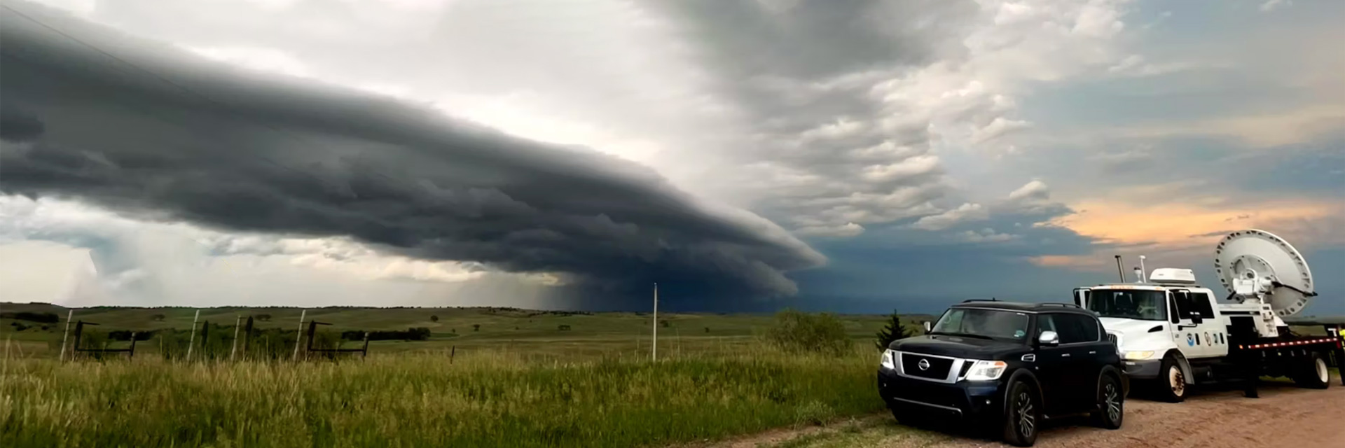 A black SUV and a radar truck stopped by the side of a road in front of a supercell.