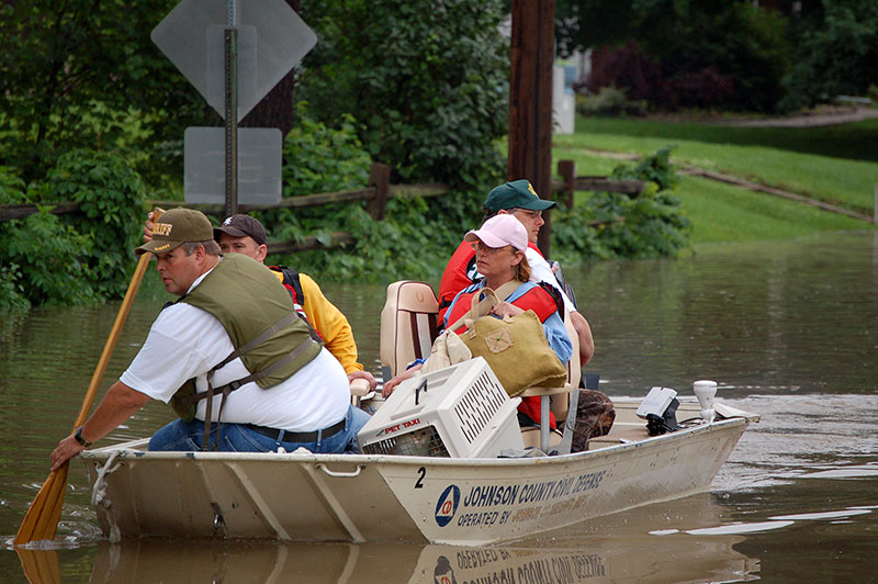 civilians being transported in a boat through flood waters by rescue personnel