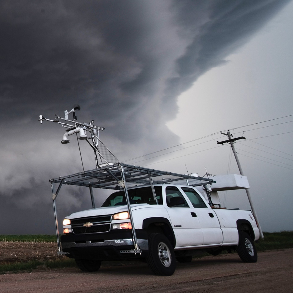 pickup truck with roof-mounted instruments in front of large thunderstorm