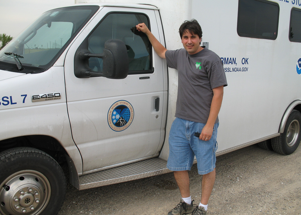 Researcher standing beside the NSSL mobile command vehicle. There is a NSSL logo on the door of the vehicle.