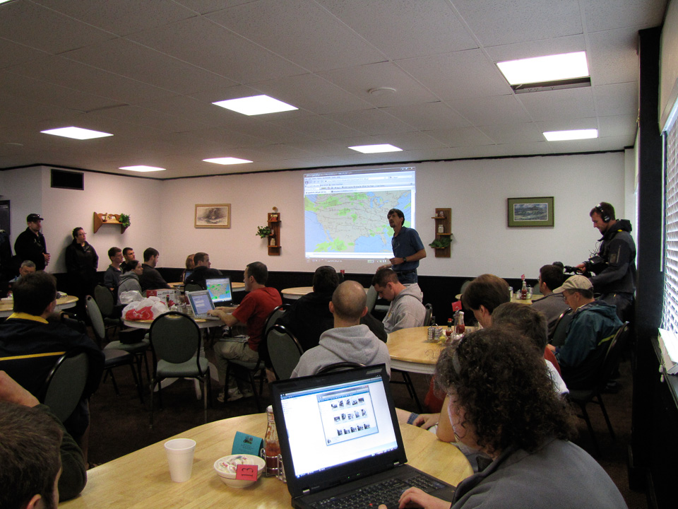 People in a motel conference room. A map of weather patterns is projected onto the wall.