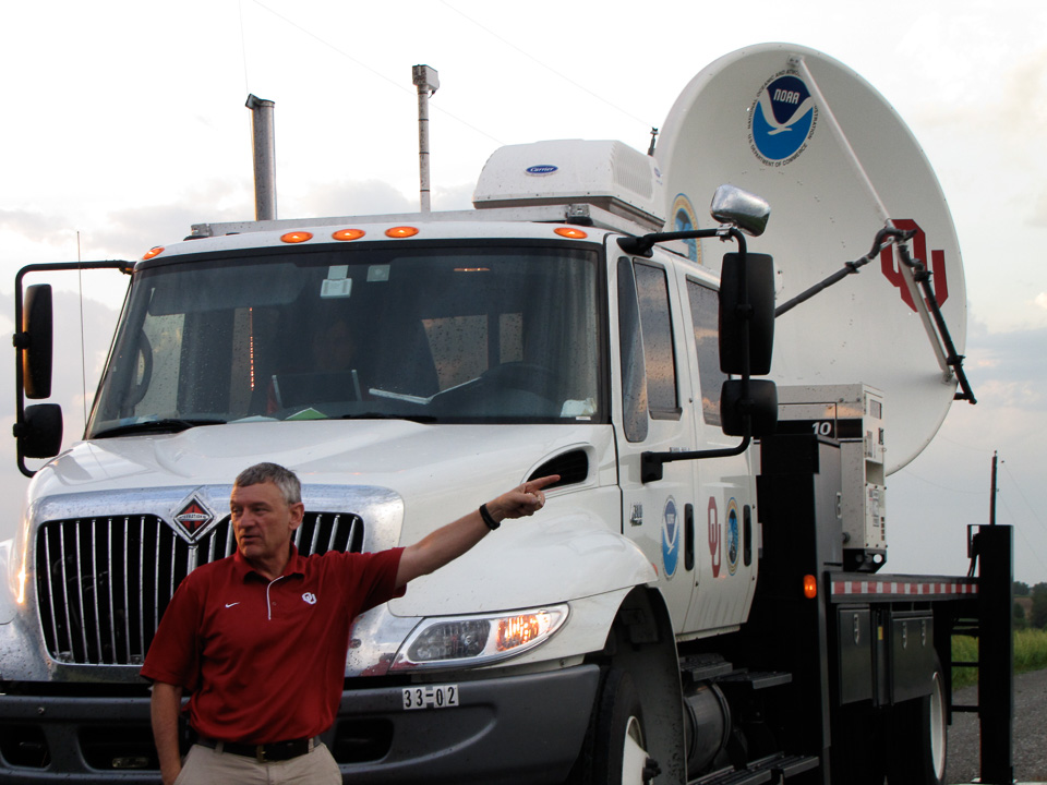 Researcher standing in front of a mobile radar truck, pointing at a storm off-camera.