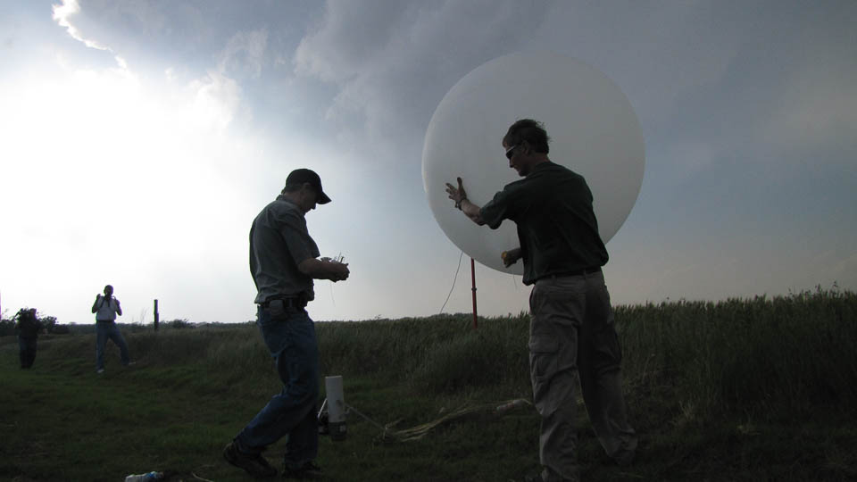 Two people launching a weather balloon at sunset.